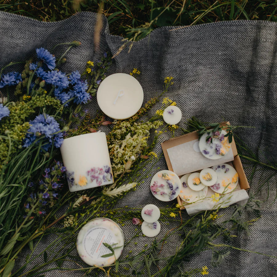 Bougie artisanale parfumée à la rose, ornée de fleurs sauvages, présentée dans un cadre naturel.
